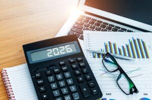 A calculator displaying '2026' sitting on a desk with financial charts representing a proactive approach to tax-smart business budgeting.