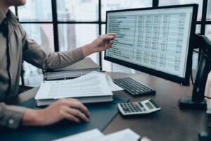 A professional accountant pointing a pen at a detailed financial spreadsheet on a computer monitor, demonstrating effective accounting for business growth through data analysis and financial planning.