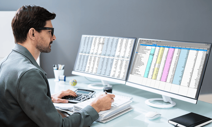 A professional accountant analyzes financial data across two large computer monitors, showcasing cloud accounting advantages like real-time data visualization.