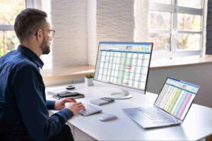 Corporate accounting Canada professional reviewing financial spreadsheets and business data on desktop and laptop computers.